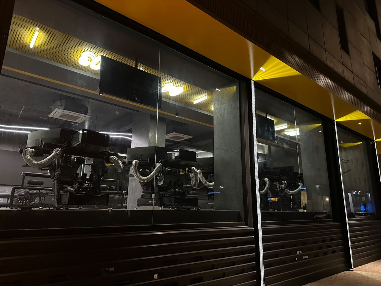 Sim rigs seen through the venue window, each fitted with flexible ventilation ducting