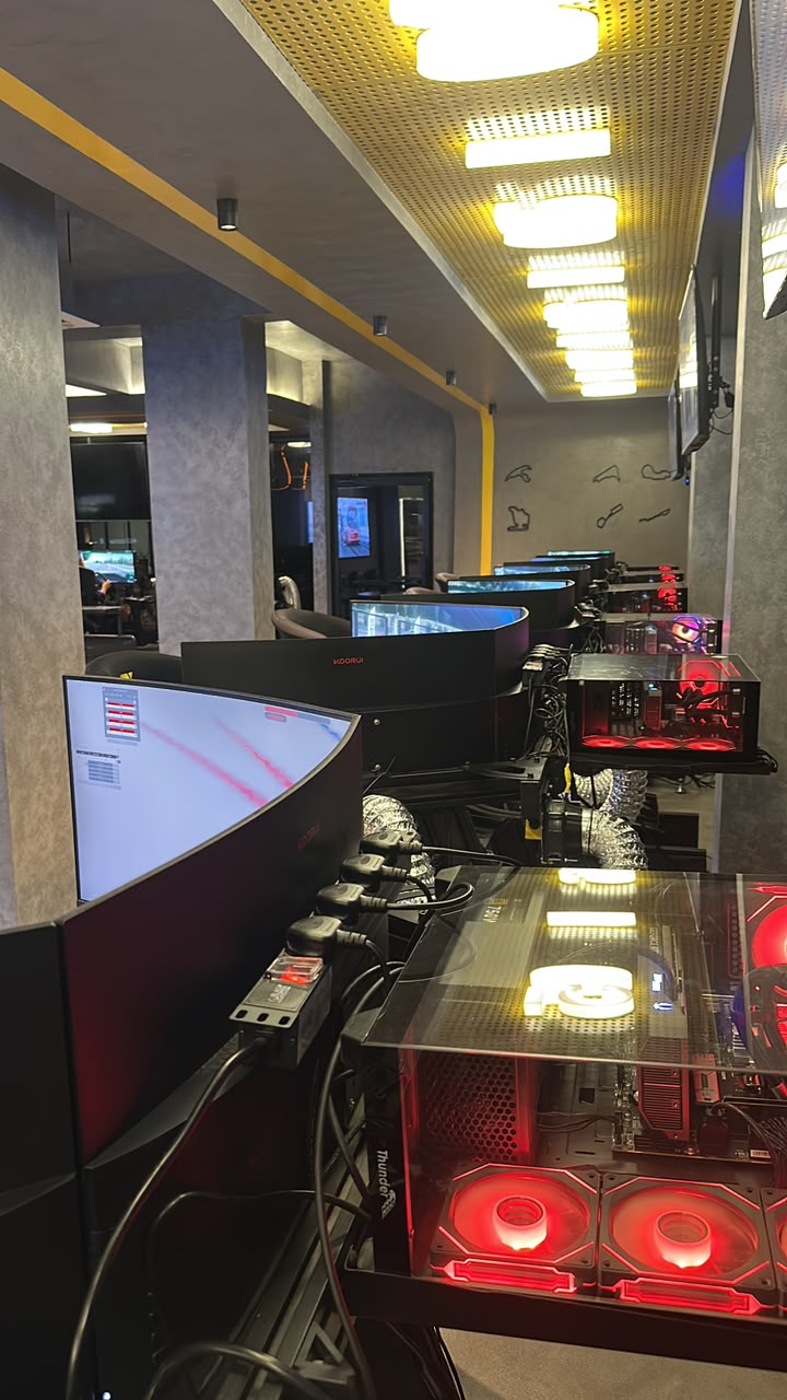 A row of sim racing stations with curved screens and red-lit PCs