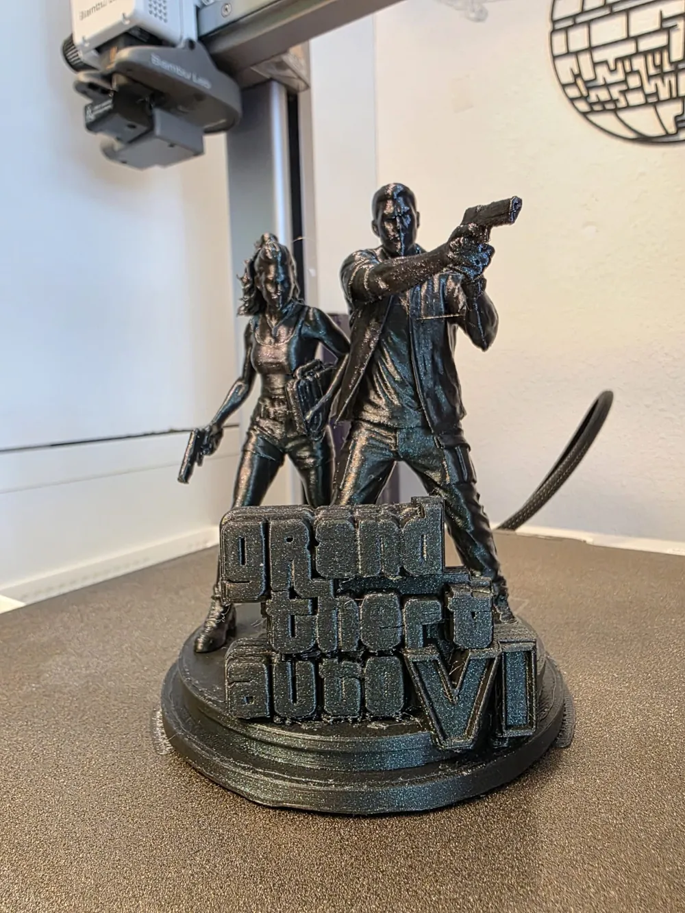 Grey-printed GTA VI statue of two characters standing on a Grand Theft Auto VI logo base